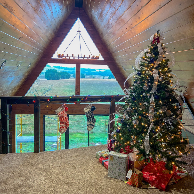 Neutral carpet in the loft of an A-frame, rustic home with a statement light fixture, Christmas tree and stockings.