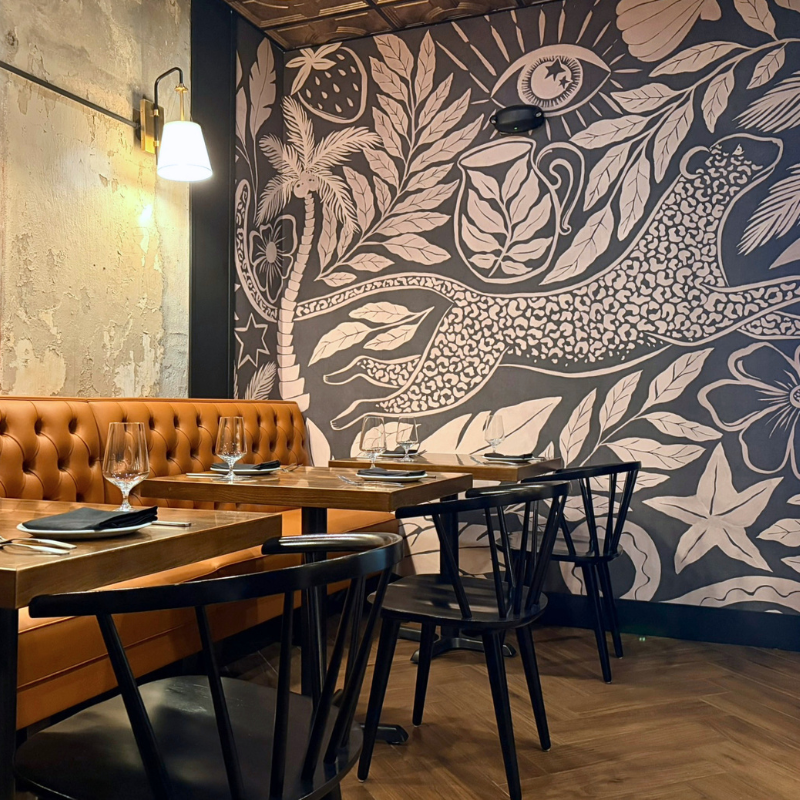 Herringbone wood-look tile on the floor of a cozy restaurant dining space with bold-patterned wallpaper.